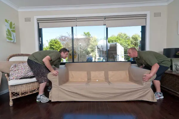 Experienced removalists from Man and His Van manoeuvring a couch through a home during a home furniture removal.