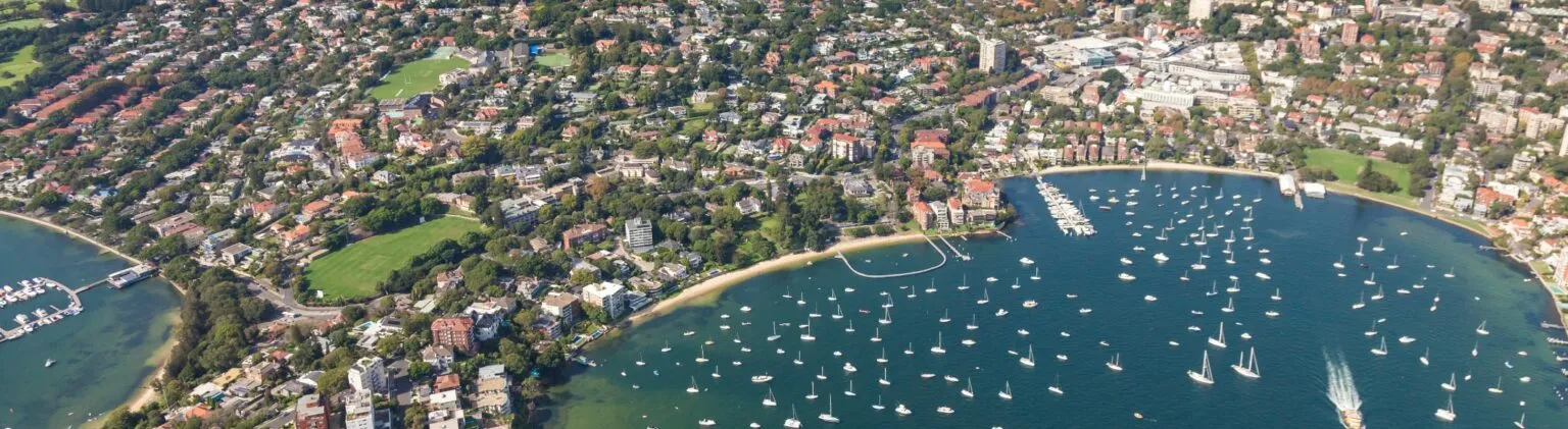 Aerial view of Double Bay with moored sailing boats, waterfront homes and leafy residential streets