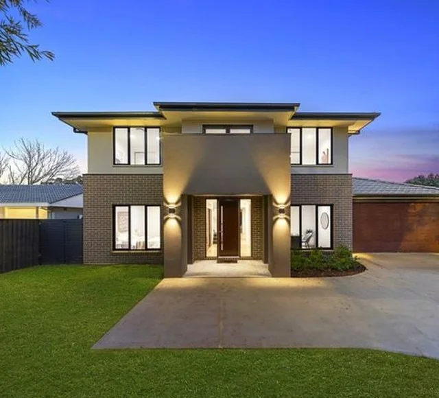 Modern two-storey home at dusk with an illuminated entrance, front lawn and driveway.