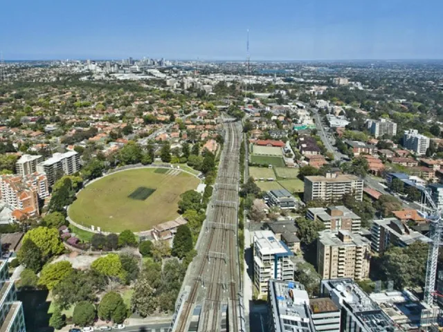 Aerial view of a sporting oval beside a railway corridor, surrounded by homes and apartment buildings