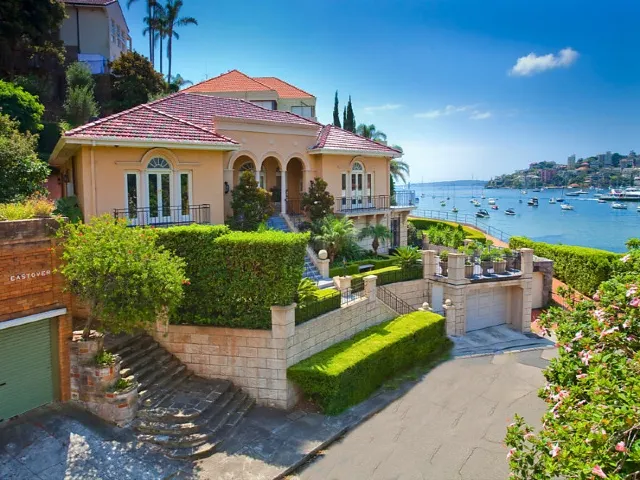 Waterfront home with arched windows, landscaped gardens and a sloping driveway overlooking the harbour